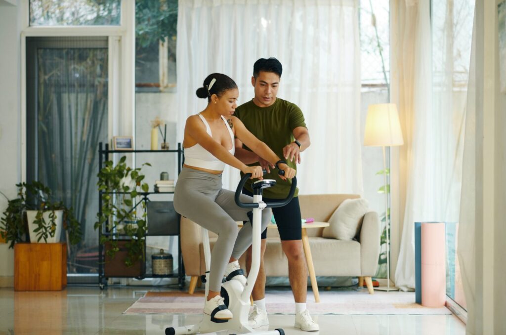 Health and wellness coach supporting a client during indoor cycling to build energy, reduce stress, and improve fitness