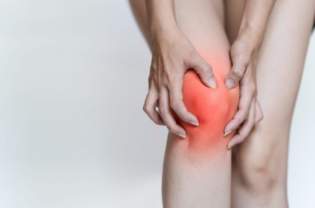 Person holding a red, swollen knee indicating joint pain or inflammation, showing early signs of knee arthritis. 