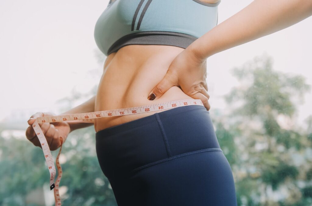 Woman measuring painful, swollen waist, showing body changes from fat disorders like lipedema